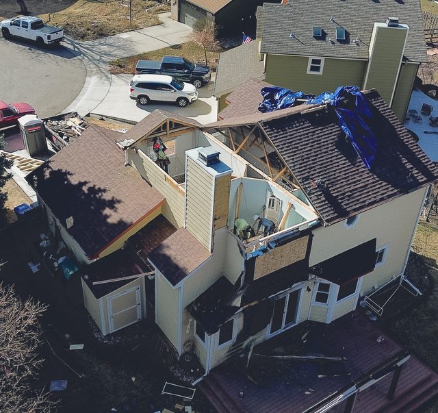 Blue tarps across the opened roof, with site vehicles alongside